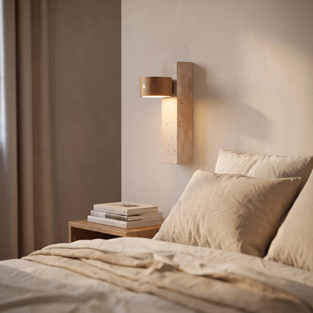 The cordless Monolith wall light glowing beside a bed, above a walnut nightstand stacked with books