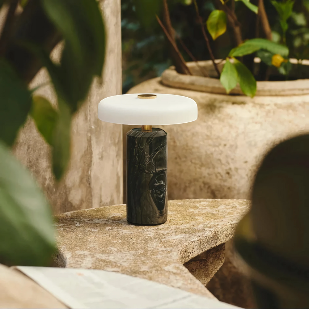 Halo charcoal marble table lamp with white shade on a stone table in a leafy courtyard, HALO-BLACK-01