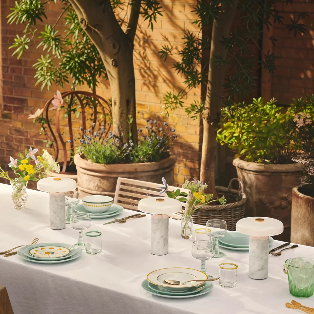 Two Halo white marble table lamps on a long outdoor dining table in a walled garden, HALO-WHITE-01