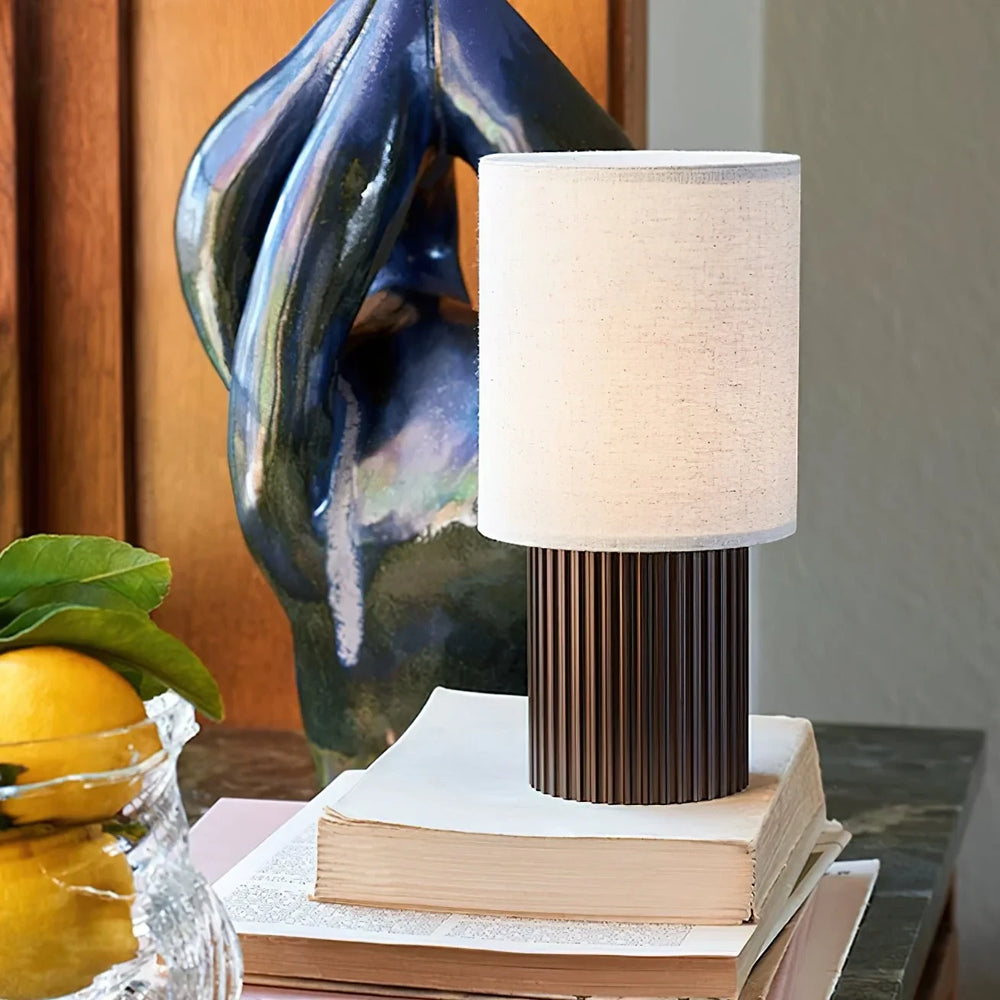 Close view of the Solene lamp's ribbed bronzed brass base, lit on a stack of books beside a ceramic sculpture