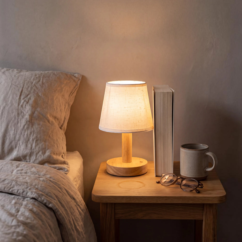 The Willow bedside lamp glowing on a nightstand beside a book, reading glasses and a linen-dressed bed