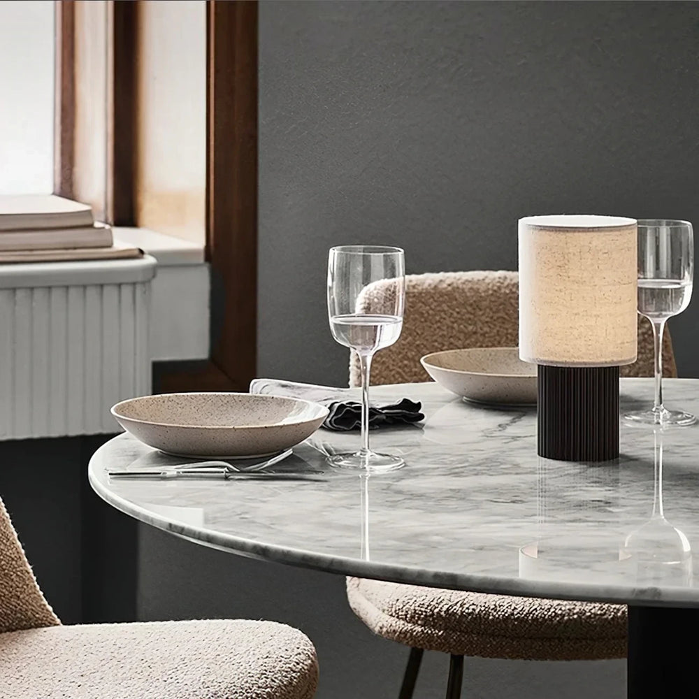 The rechargeable Solene lamp glowing on a round marble dining table between bouclé chairs