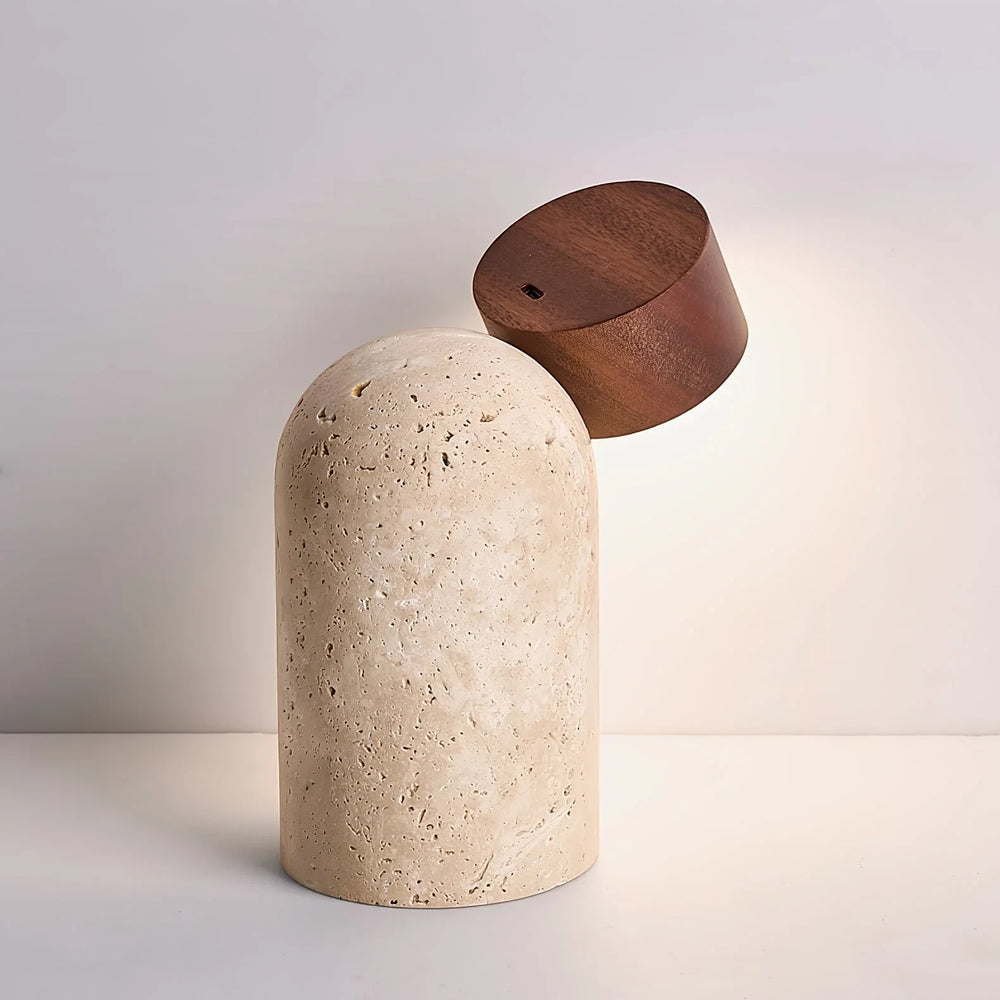 Vensalo Sten rechargeable table lamp lit, its walnut head tilted right on the domed travertine base