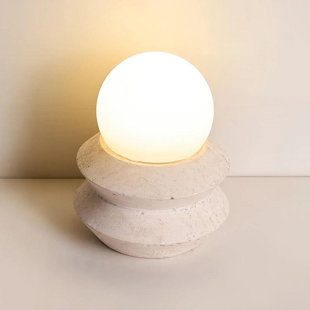 The cordless Solace mushroom lamp, opal globe resting on a stacked travertine base, casting a warm glow