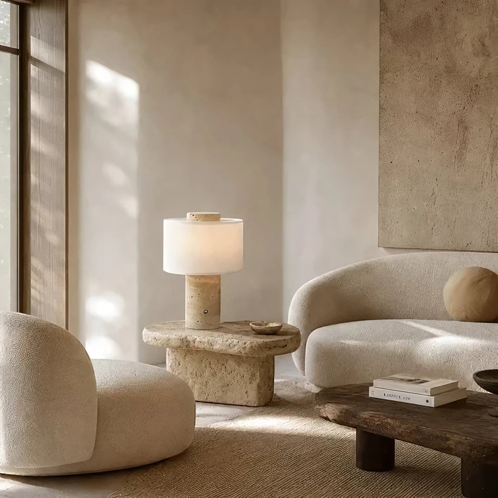 The cordless Onyx Cloud lamp glowing on a travertine table in a calm, sunlit living room