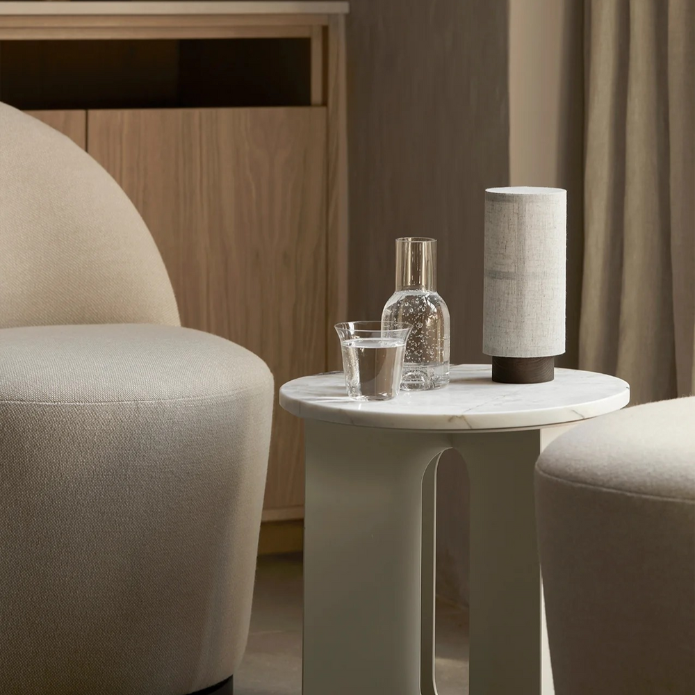 The cordless Washi lamp lit on a marble side table beside a glass carafe in a calm living room