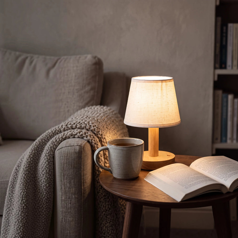 Warm light from the cordless Willow lamp on a side table beside a sofa, with a mug of tea and an open book