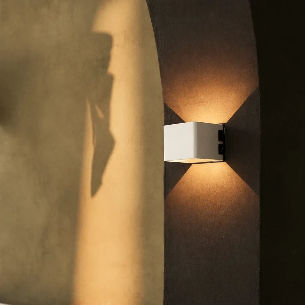 The Cubo wall light glowing on a curved plaster wall, casting light in two cones above and below