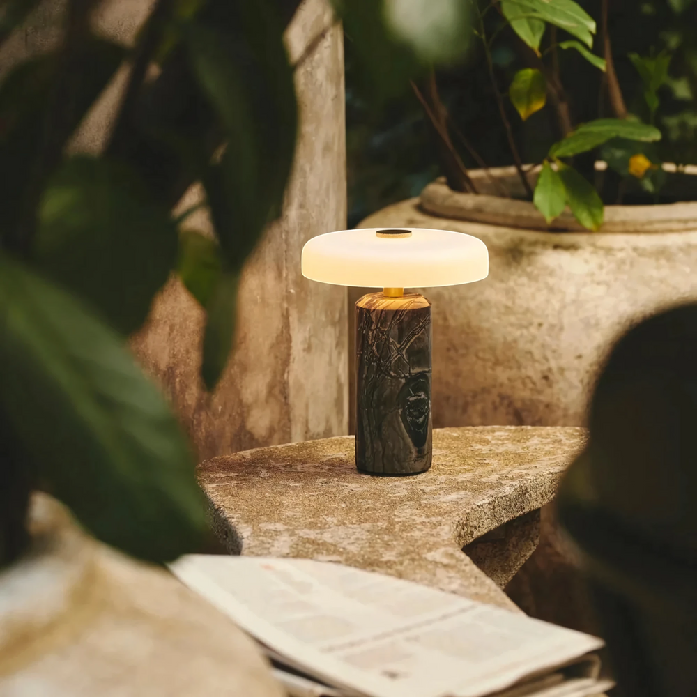 Halo charcoal marble table lamp glowing warmly on a stone garden table at dusk, HALO-BLACK-01