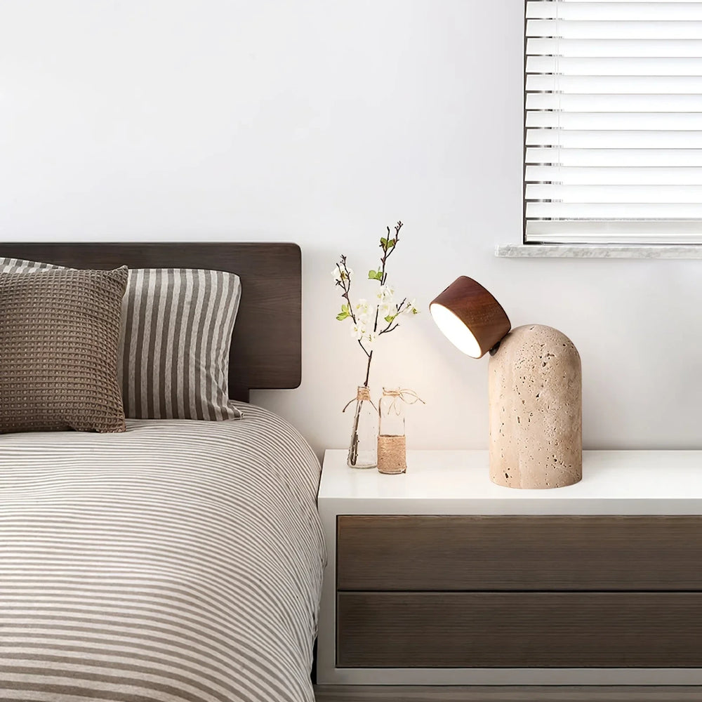 The rechargeable Sten lamp glowing on a bedside table beside striped bedding and a window