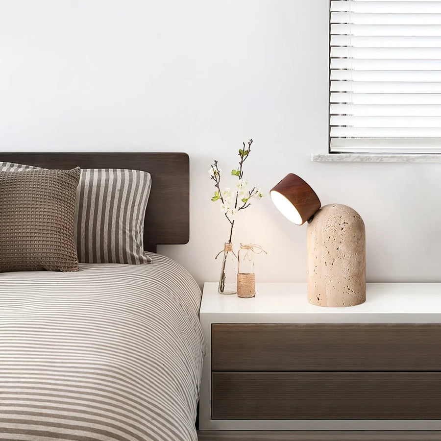 The rechargeable Sten lamp glowing on a bedside table beside striped bedding and a window