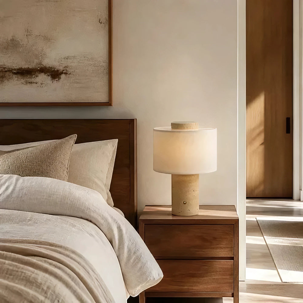 The rechargeable Onyx Cloud lamp lit on a wooden nightstand beside a bed and framed artwork