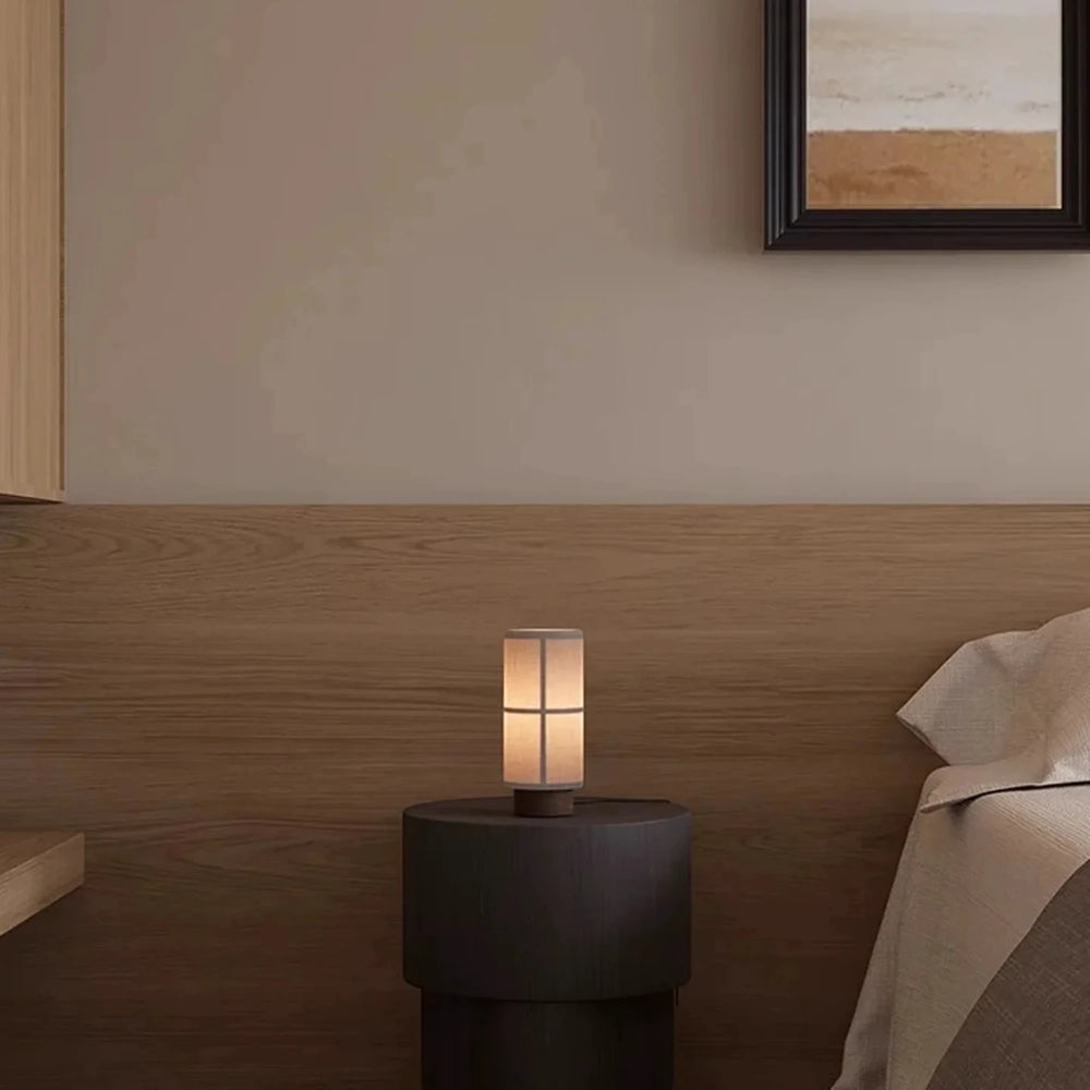 The rechargeable Washi lamp glowing warm on a round nightstand beside a wooden headboard