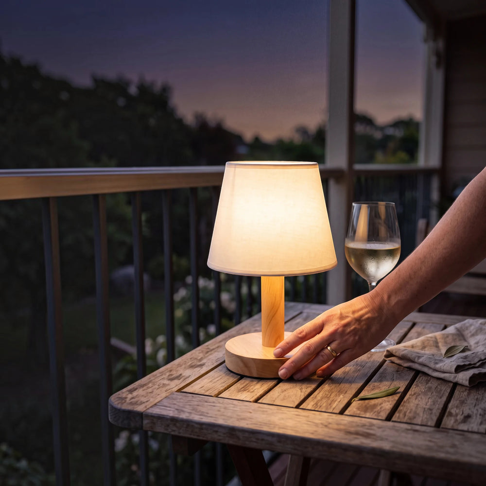 A hand touching the wooden base of the Willow lamp to dim its warm white light